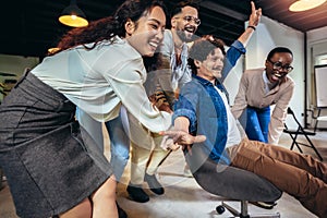 Businesspeople in smart casual wear having fun while racing on office chairs and smiling