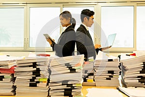 Businesspeople standing back-to-back with pile of paper work in foreground.