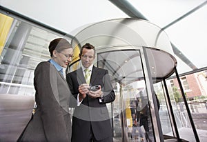 Businesspeople Using PDA In Front Of Revolving Door photo