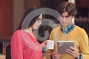 Businesspeople using tablet computer, talking in office.