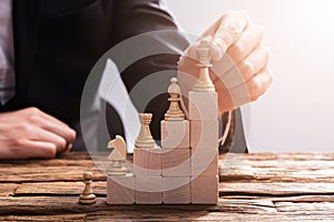 Businessperson Arranging Chess Piece On Wooden Blocks