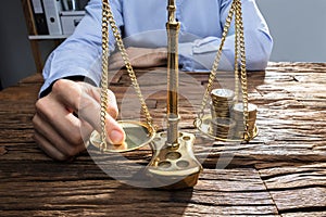 Businessperson Balancing Coins On Justice Scale With His Finger