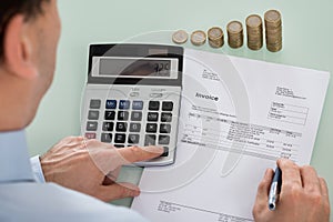 Businessperson Calculating Invoice With Coins At Desk