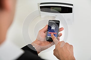 Businessperson Disarming Security System With Mobile Phone