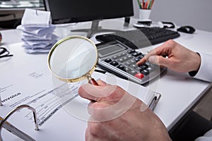 Businessperson Examining Invoice Through Magnifying Glass