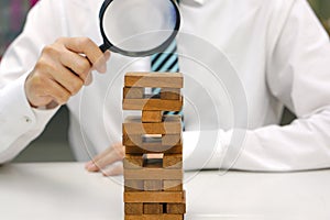 Businessperson hand holding glass magnifying over wooden blocks tower or building. Concept of risk management.