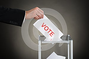 Businessperson Hand Putting Vote Into A Ballot Box