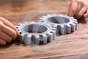 Businessperson Joining Gears On Desk