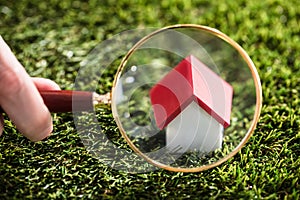 Businessperson Looking At House Model Through Magnifying Glass