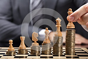 Businessperson Placing Chess Pieces On Stacked Coins