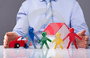 Businessperson Protecting Human Figures, House Model And Car