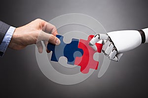 Businessperson And Robot Holding Jigsaw Puzzle