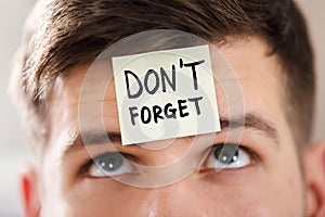 Sticky Note With Don`t Forget Text Stuck On Man`s Forehead photo