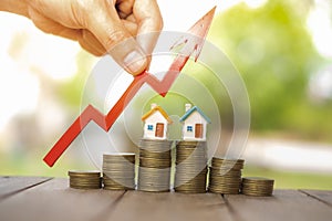 Businessperson`s Hand Holding Arrow Over Stacked Coins With House Models. Home model and arrow graph with growing. Business