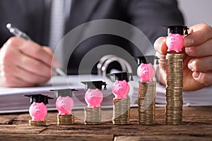 Businessperson Placing Piggybank With Graduation Cap