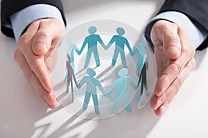 Businessperson`s Hand Protecting Paper Cut Out Figures