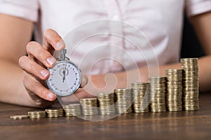 Businessperson With Stopwatch And Stack Of Coins