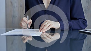 Businessperson woman in dark blue blouse analyzing document at glass desk. Close-up of a professional auditor or lawyer