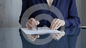Businessperson woman in dark blue blouse analyzing document at glass desk. Close-up of a professional auditor or lawyer