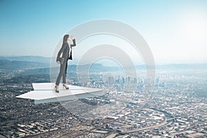 Businesswoman on abstract paper plane looking into the distance on creative bright sky background with mock up place. Future,