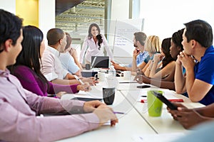 Businesswoman Addressing Meeting Around Boardroom Table