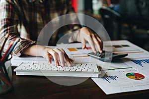 Businesswoman analyzing financial reports with calculator and typing on modern computer keyboard at office. Business analytics