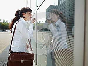 Businesswoman Applying Makeup Lipstick On Street Using Office Window