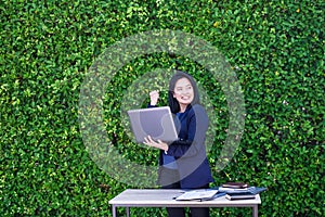 Businesswoman arm up to celebrating business plan success outside office at green leaf wall