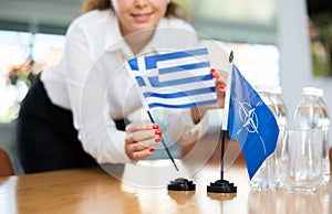 Businesswoman arranging the flags of NATO (OTAN) and Greece for presentation and negotiations