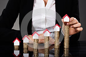 Businesswoman Arranging House Model On Stacked Coins