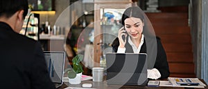 Businesswoman in black suit talking on mobile phone and sitting with her male colleague.