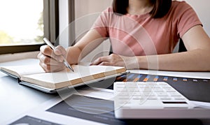 Businesswoman bookkeeper hand note analysis the graph with calculator and laptop at the home office for setting challenging