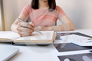 Businesswoman bookkeeper hand note analysis the graph with calculator and laptop at the home office for setting challenging