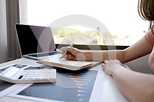 Businesswoman bookkeeper hand note analysis the graph with calculator and laptop at the home office for setting challenging