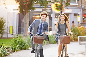 Businesswoman And Businessman Riding Bike Through City Park