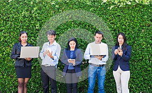 Businesswoman and businessman working outside office using laptop computer mobile phone and tablet device at green leaf