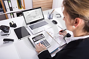 Businesswoman Calculating Invoice Using Calculator And Laptop