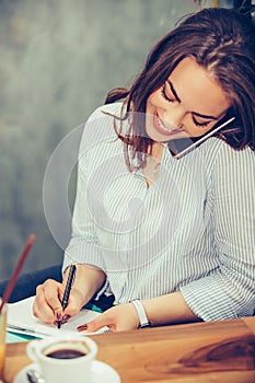 Businesswoman calling on mobile phone and taking notes