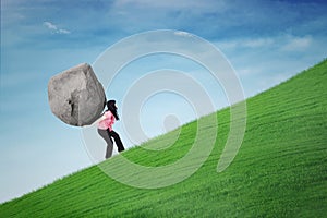 Businesswoman carrying stone on the hill