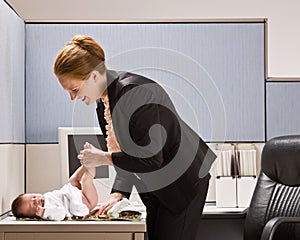 Businesswoman changing baby diaper at desk