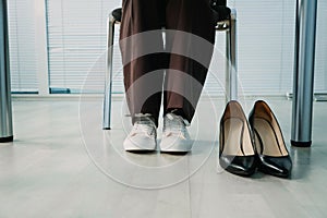 Businesswoman changing uncomfortable black high heels on comfortable white sneakers in office.