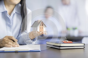 Businesswoman choosing mini house model from model on wood table