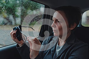 Businesswoman cleaning eyeglasses at backseat of a car during rain