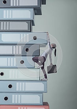 Businesswoman climbing a pile of ring binders