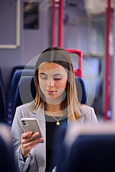 Businesswoman Commuting To Work On Train Looking At Mobile Phone