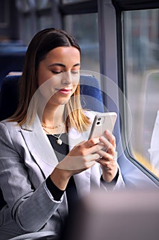 Businesswoman Commuting To Work On Train Looking At Mobile Phone