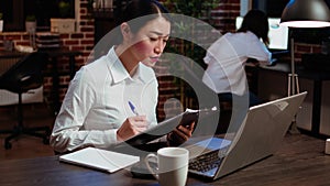 Businesswoman crosschecking data between laptop and paperwork