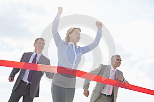 Businesswoman crossing finishing line with colleagues in background