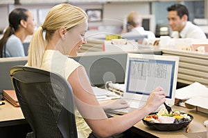 Businesswoman in cubicle using laptop and eating s photo
