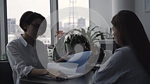 Businesswoman discusses contract rules with woman job candidate and looks through her portfolio. Close-up.